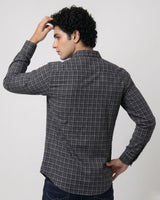 A man wearing a dark gray and black plaid long-sleeve shirt, shown from the back against a light gray studio background.