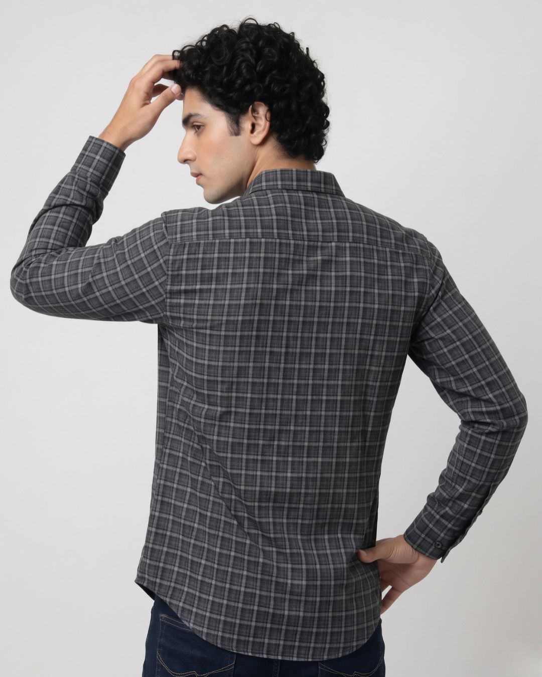 A man wearing a dark gray and black plaid long-sleeve shirt, shown from the back against a light gray studio background.