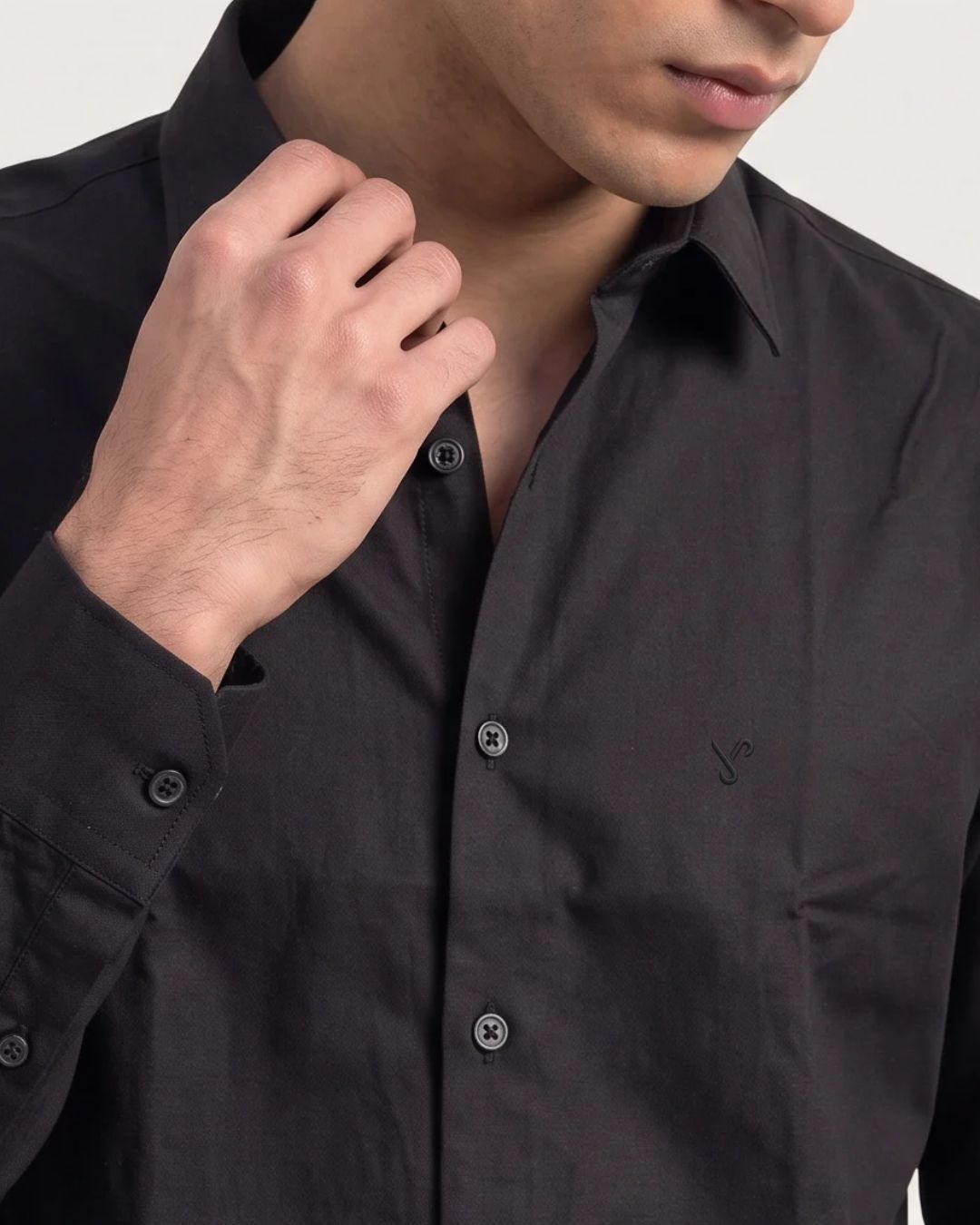 Close-up of a man wearing a dark charcoal gray button-down shirt, adjusting the collar with one hand.