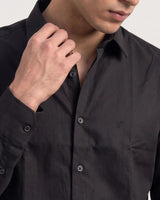 Close-up of a man wearing a dark charcoal gray button-down shirt, adjusting the collar with one hand.