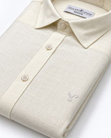 A folded cream-colored linen shirt by Yellow Pepper, featuring a textured weave, a classic collar, and a small embroidered logo on the chest.