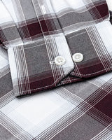 Close-up of a plaid button-up shirt showing the folded cuff with white buttons, featuring a pattern of white, gray, and dark burgundy plaid.