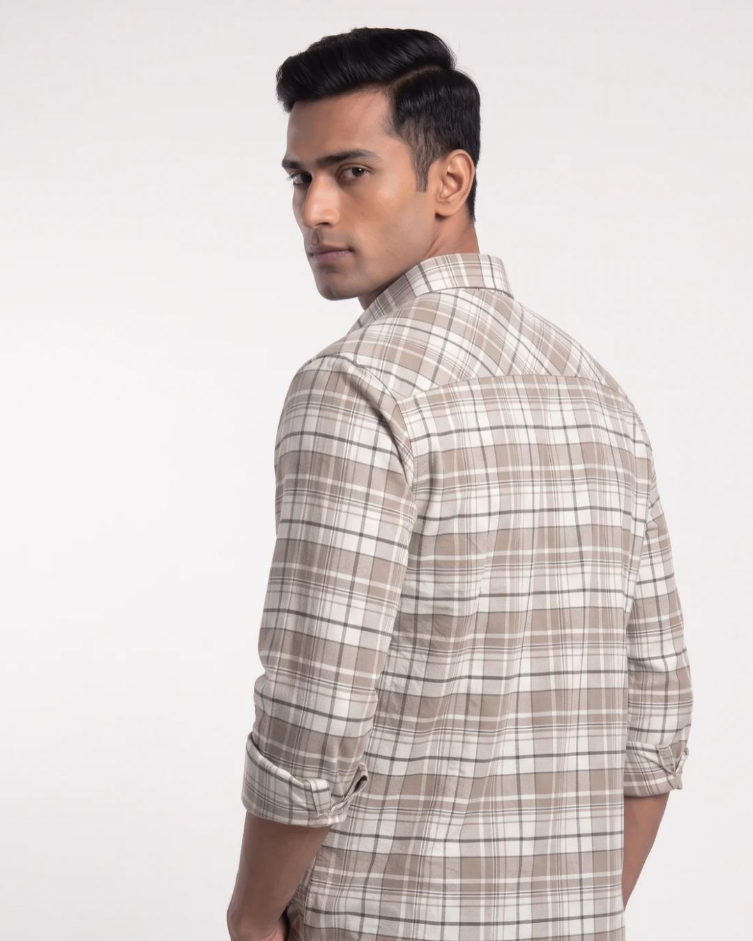 A man wearing a beige and white plaid long-sleeve shirt, shown from a three-quarter back view against a plain light gray studio background.