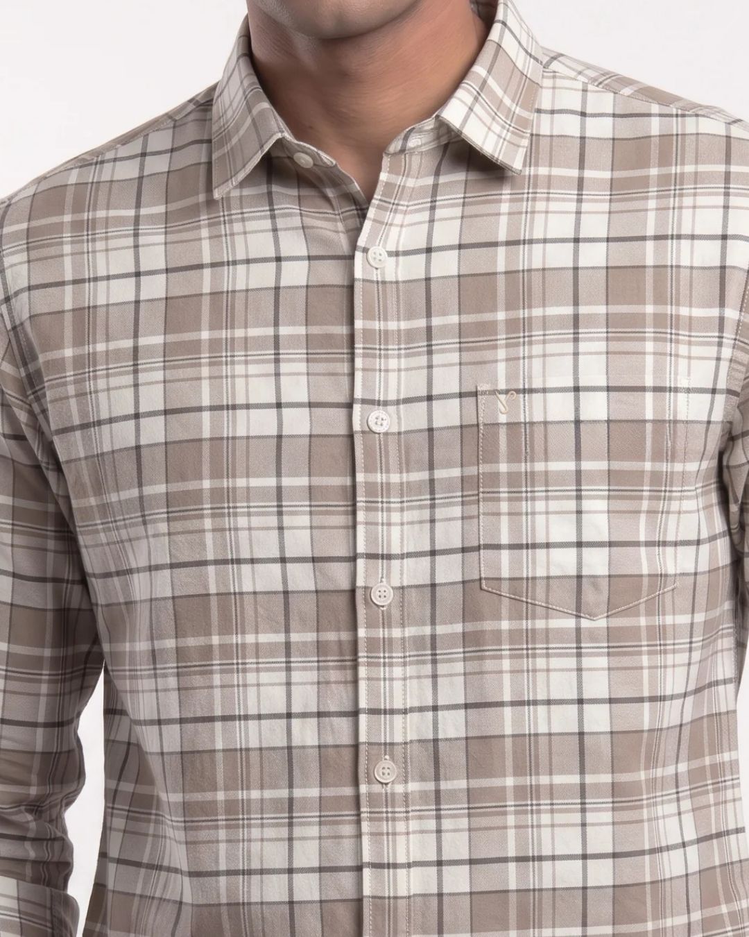A close-up of a man wearing a long-sleeve button-down shirt with a brown, beige, and white plaid pattern. The shirt features a classic collar, white buttons, and a chest pocket with a small embroidered logo.