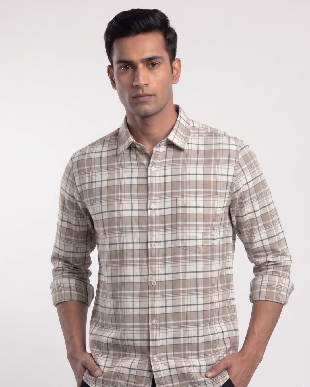 A man wearing a beige and brown plaid long-sleeve button-up shirt, standing against a light gray studio background.