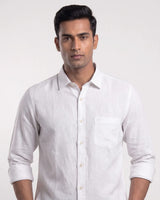 A man wearing a white long-sleeve linen shirt with a chest pocket, shown from the waist up against a light gray studio background.