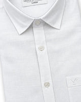 Close-up of a white long-sleeve button-down shirt with a pointed collar, white buttons, and a chest pocket featuring a small embroidered logo.