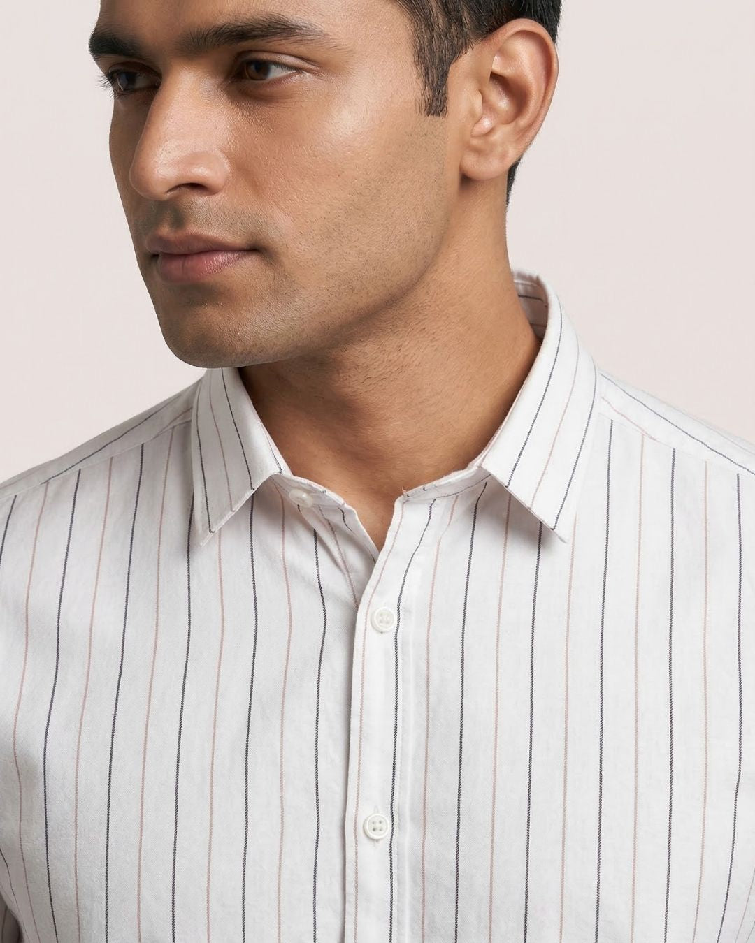 Man wearing a light-colored striped shirt against a plain background