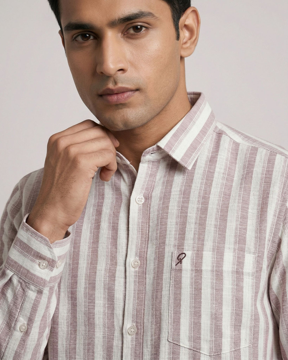 Man wearing a striped shirt with a visible brand logo on a plain background