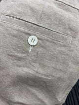 Close-up detail of a light beige textured fabric garment, showing a stitched pocket and a single white button.