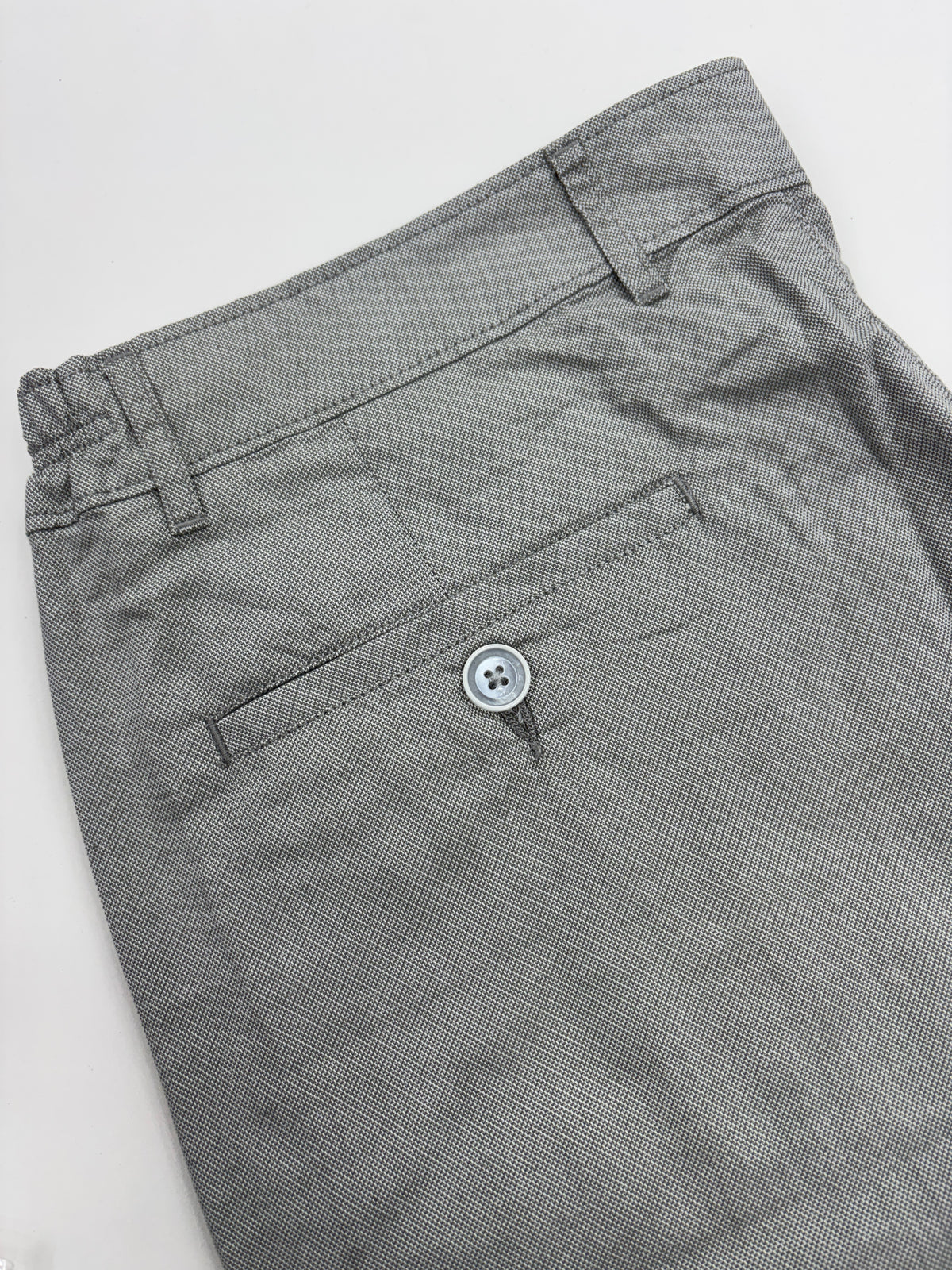 Close-up of gray trousers showing the waistband, belt loops, and a side pocket with a single visible button.