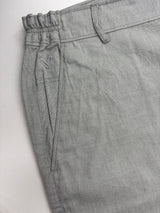 Close-up of light gray textured trousers showing the elastic waistband, belt loops, and side pocket with a small embroidered logo.