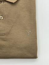 Close-up of a folded tan knit polo shirt showing the collar, button placket, pocket, and a small embroidered logo on a white background.