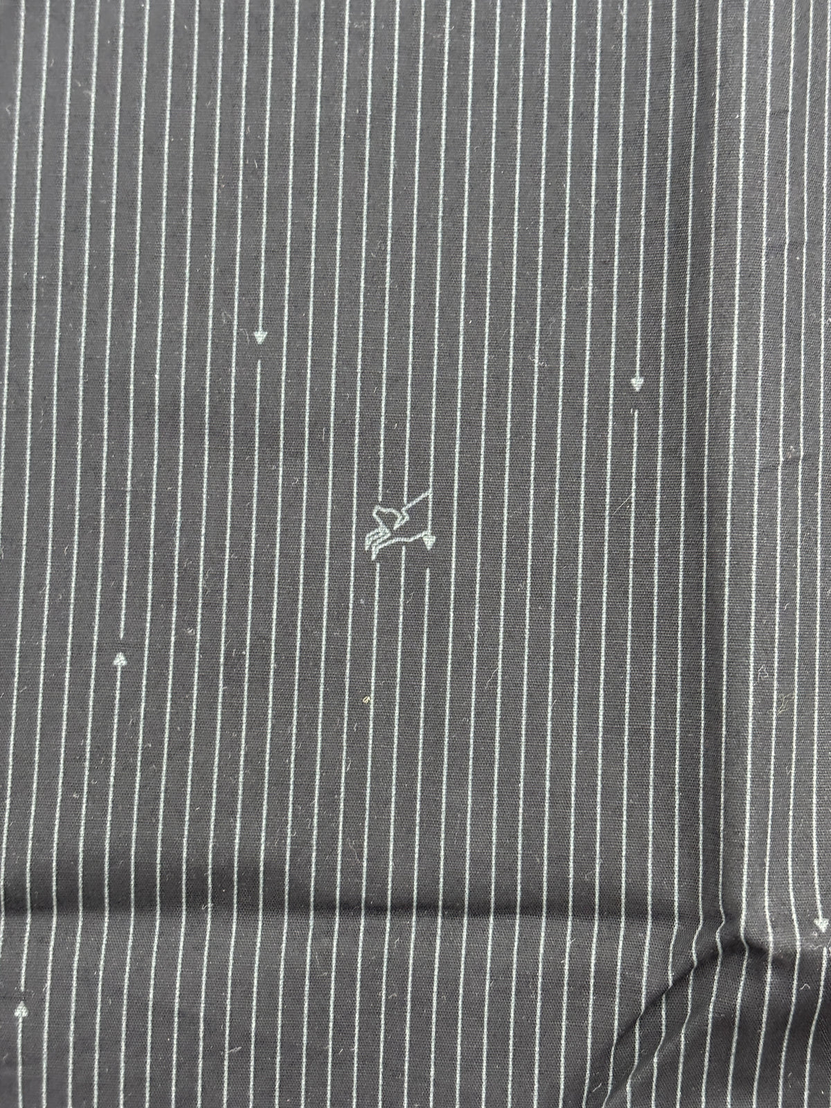 A close-up of a dark gray pinstriped fabric with thin white vertical stripes and a small white embroidered logo in the center.