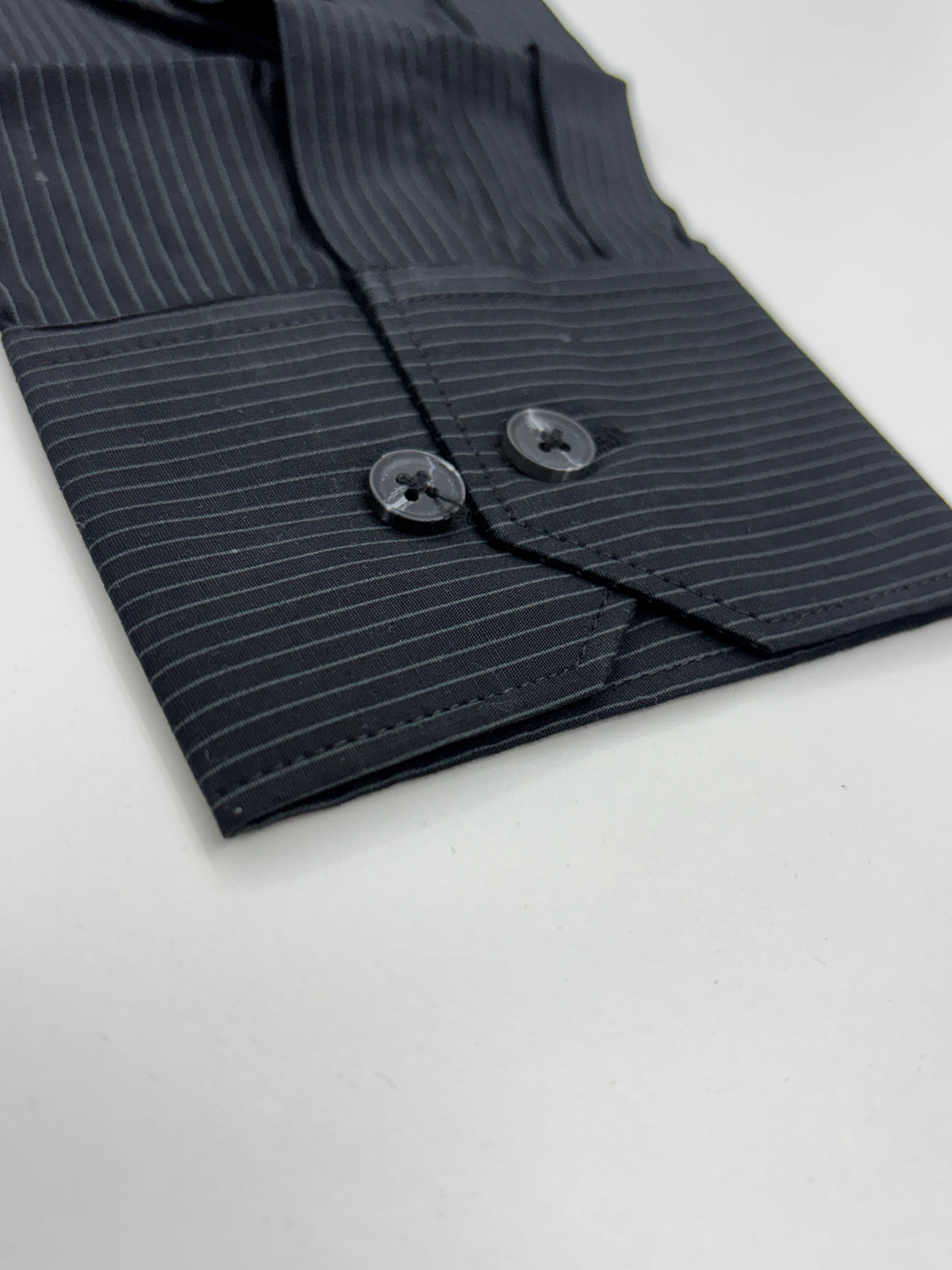 Close-up of a dark navy pinstriped shirt cuff with two dark buttons, laid flat on a white surface.