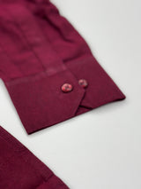 Close-up of a burgundy or deep wine-colored fabric garment, showing the cuff with two matching decorative buttons on a white background.