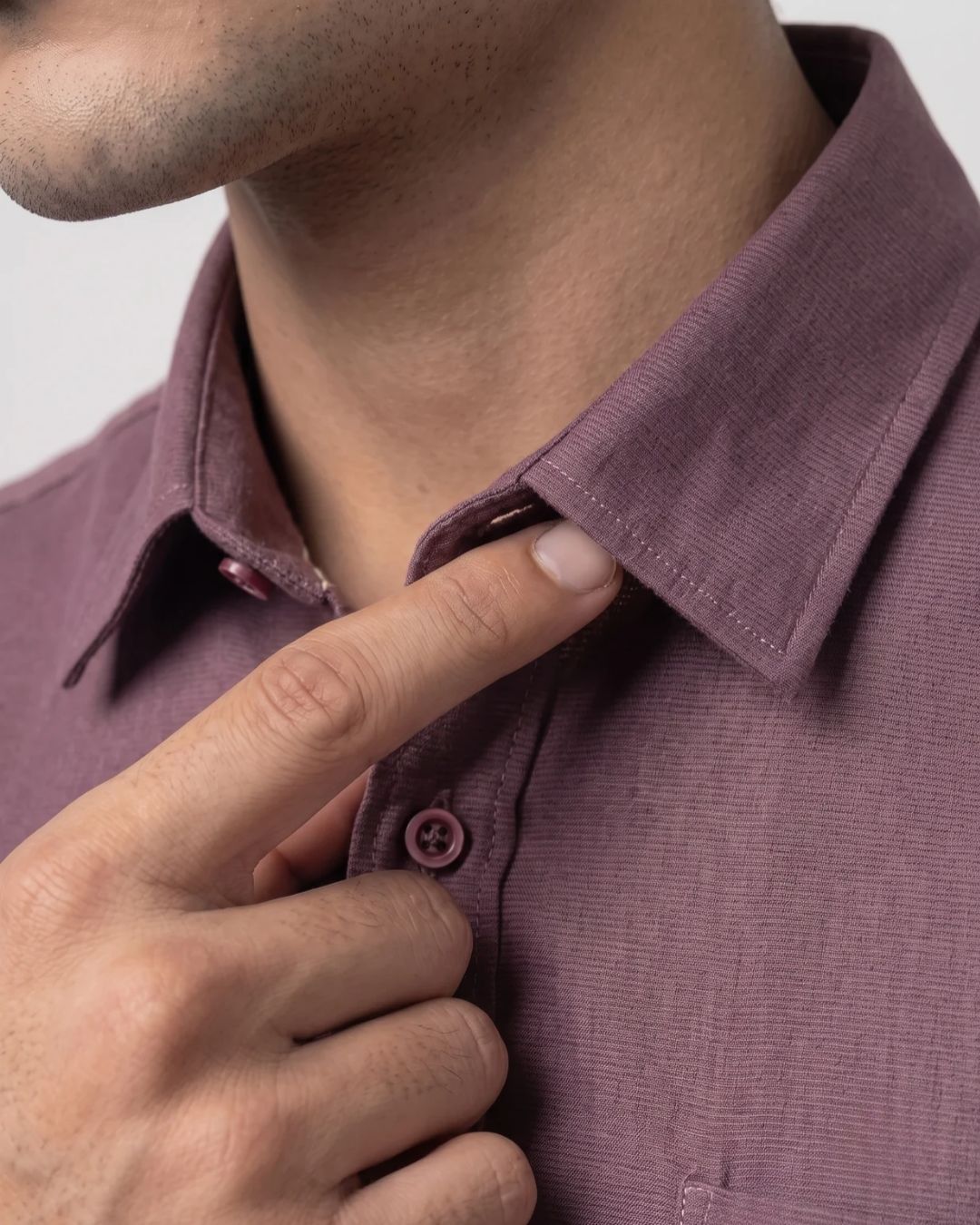 Close-up of a man wearing a textured mauve-purple collared button-up shirt, with his hand adjusting the collar.