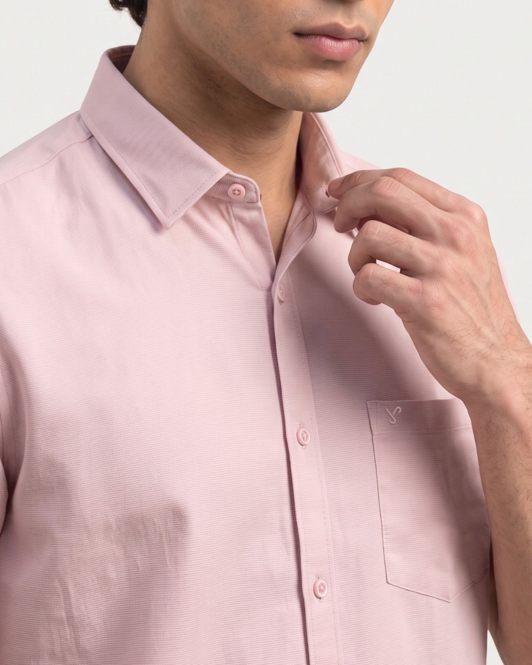 A close-up of a man wearing a light pink long-sleeve button-down shirt, adjusting the collar with one hand.