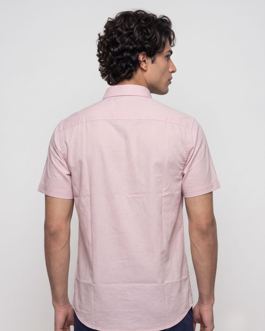 A man wearing a light pink short-sleeve button-down shirt, shown from the back against a plain light gray studio background.