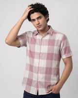 A man wearing a short-sleeve button-up shirt with a pink and off-white checkered pattern, posed against a light gray studio background.
