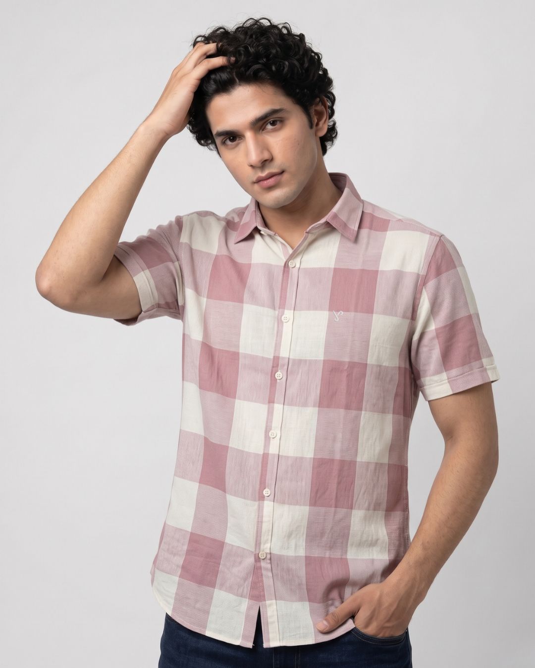 A man wearing a short-sleeve button-up shirt with a pink and off-white checkered pattern, posed against a light gray studio background.