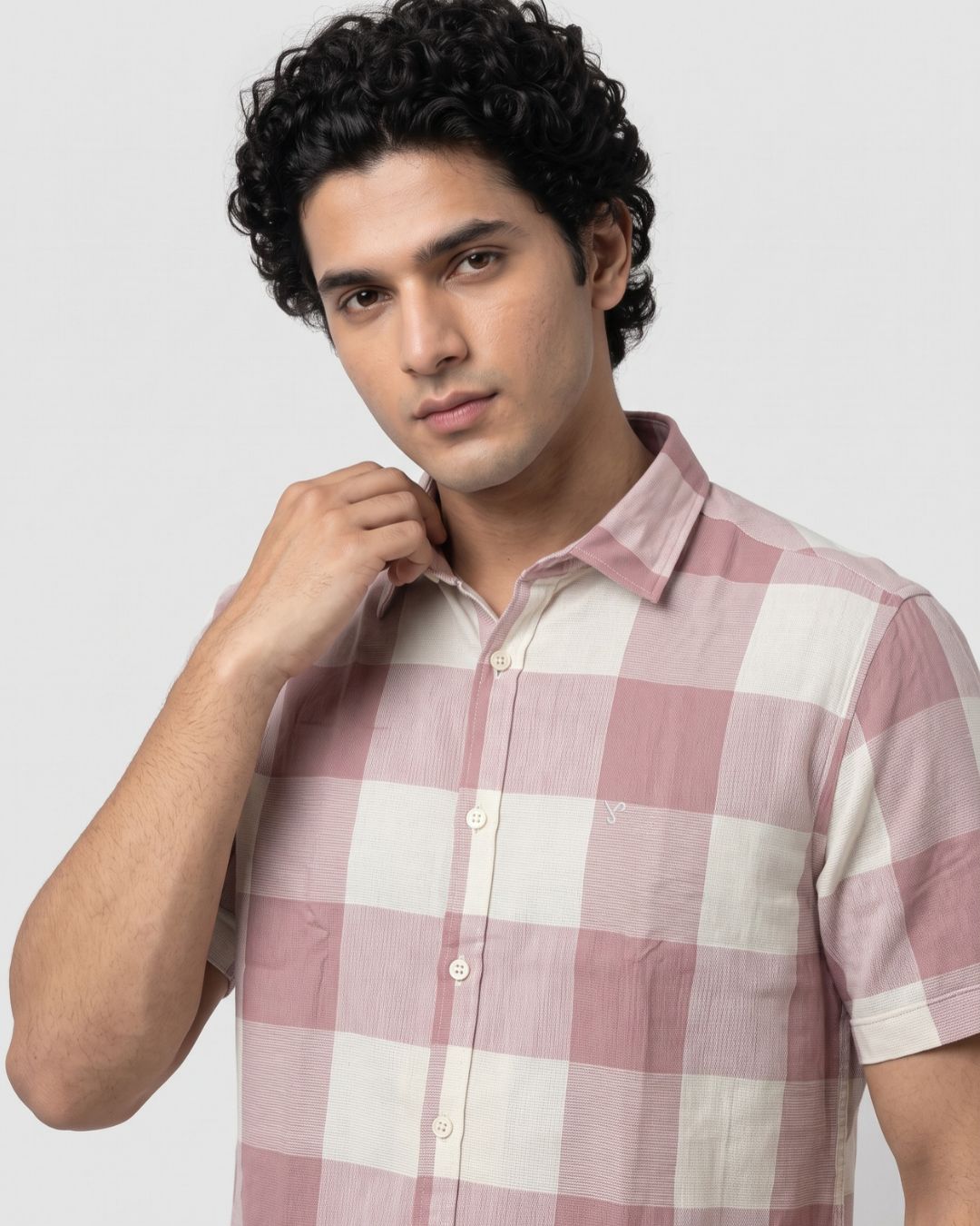 A man wearing a short-sleeve button-up shirt with a pink and off-white checkered pattern, posed against a light gray background.