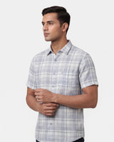 A man wearing a short-sleeve button-up plaid shirt in light gray and white, photographed against a plain light gray studio background.