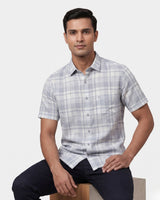 A man wearing a short-sleeve plaid button-down shirt in light gray and white, shown from a three-quarters back view against a light gray background.