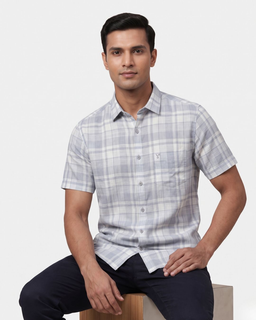 A man wearing a short-sleeve plaid button-down shirt in light gray and white, shown from a three-quarters back view against a light gray background.