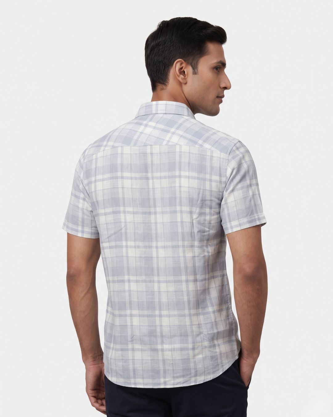 A man wearing a short-sleeve plaid button-down shirt in light gray and white, shown from a three-quarters back view against a light gray background.