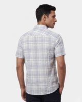 A man wearing a short-sleeve plaid button-down shirt in light gray and white, shown from a three-quarters back view against a light gray background.