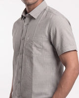 A man wearing a light gray short-sleeve button-up shirt with thin vertical pinstripes and a chest pocket, shown from the neck down against a plain white background.