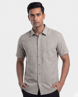 A man wearing a short-sleeve button-up shirt with a fine vertical stripe pattern in beige and gray, posed against a plain light gray background.