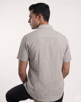 A man wearing a light gray and white vertically striped short-sleeve button-up shirt, shown from the back against a plain white studio background.