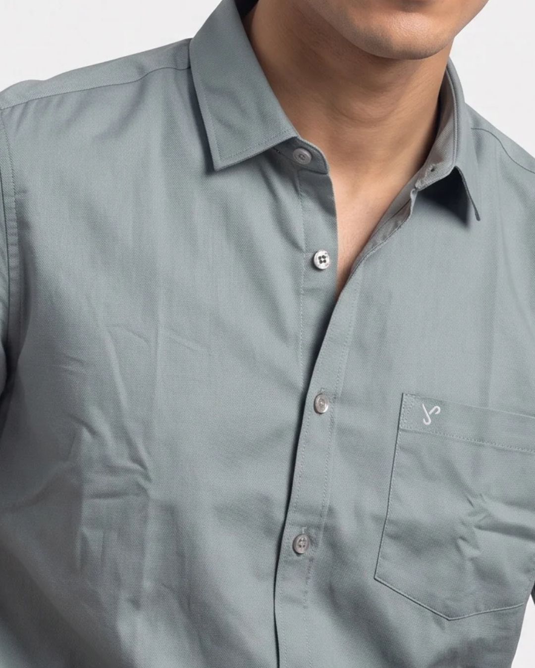 Close-up of a man wearing a muted sage green button-down shirt with a chest pocket and a small embroidered logo.