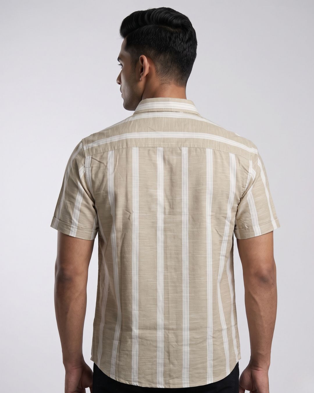 A man viewed from the back wearing a short-sleeve button-up shirt with vertical beige and white stripes, set against a plain light gray studio background.