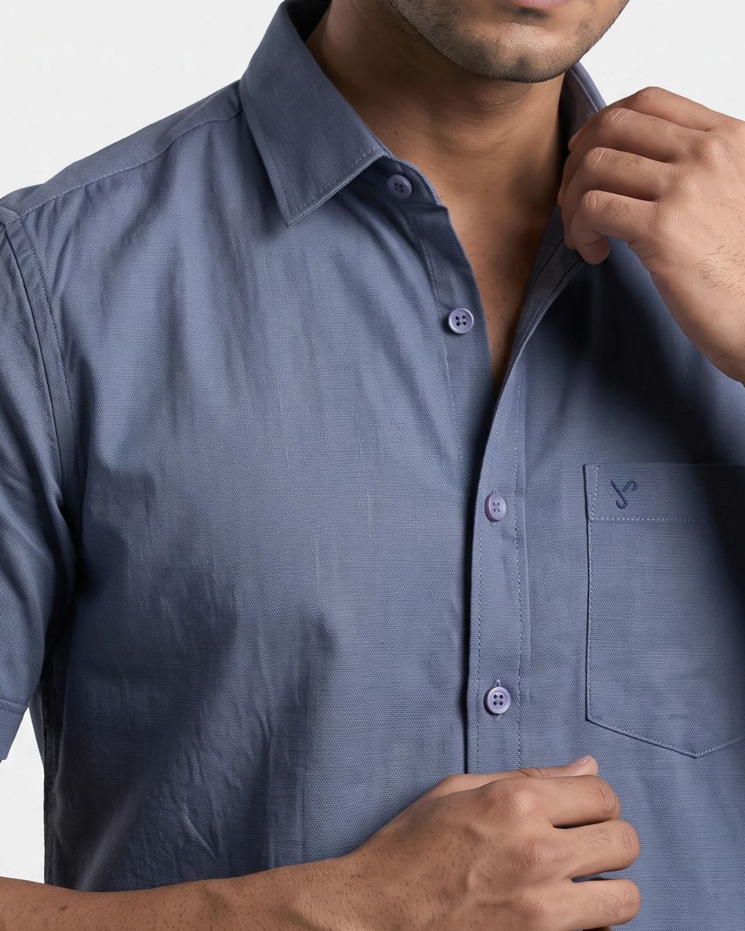 A close-up of a man wearing a slate blue short-sleeve button-down shirt with a chest pocket and a small embroidered logo.
