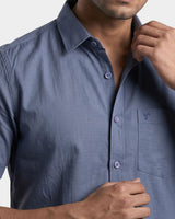 A close-up of a man wearing a slate blue short-sleeve button-down shirt with a chest pocket and a small embroidered logo.