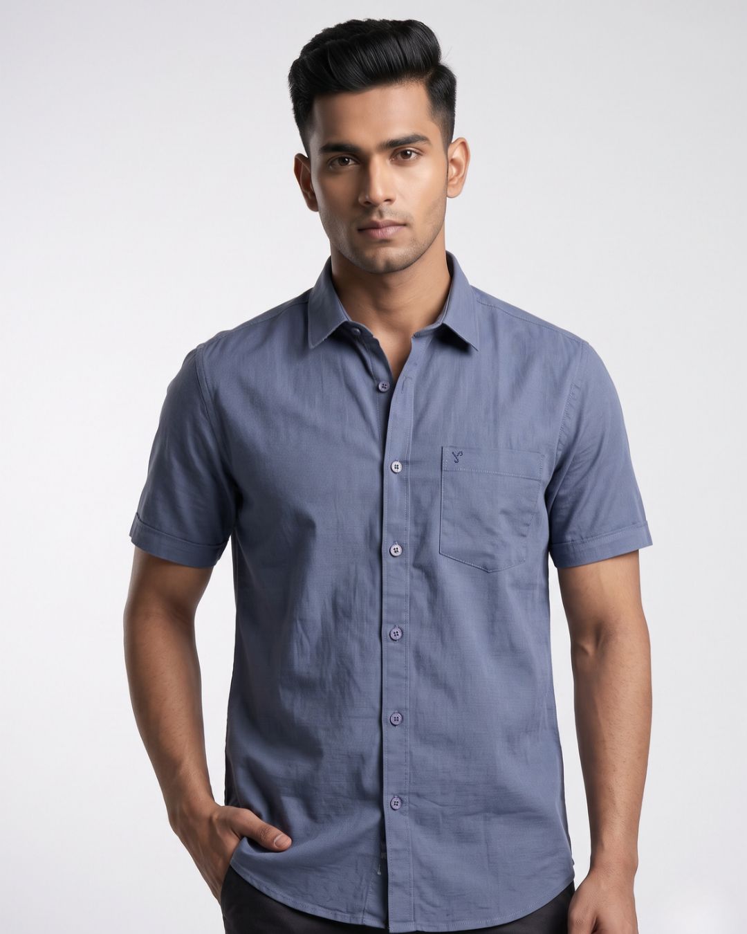 A man wearing a short-sleeve button-down shirt in slate blue, photographed against a light gray studio background.