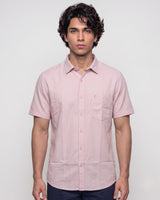 A man wearing a light pink short-sleeve button-up shirt with a chest pocket, photographed against a plain light gray studio background.