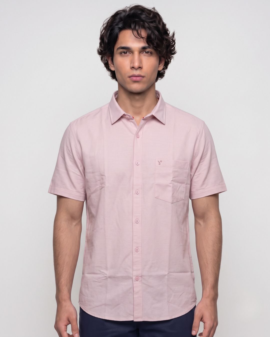 A man wearing a light pink short-sleeve button-up shirt with a chest pocket, photographed against a plain light gray studio background.