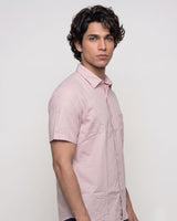 A man wearing a light pink short-sleeve button-up shirt, shown from a side profile against a plain light gray studio background.