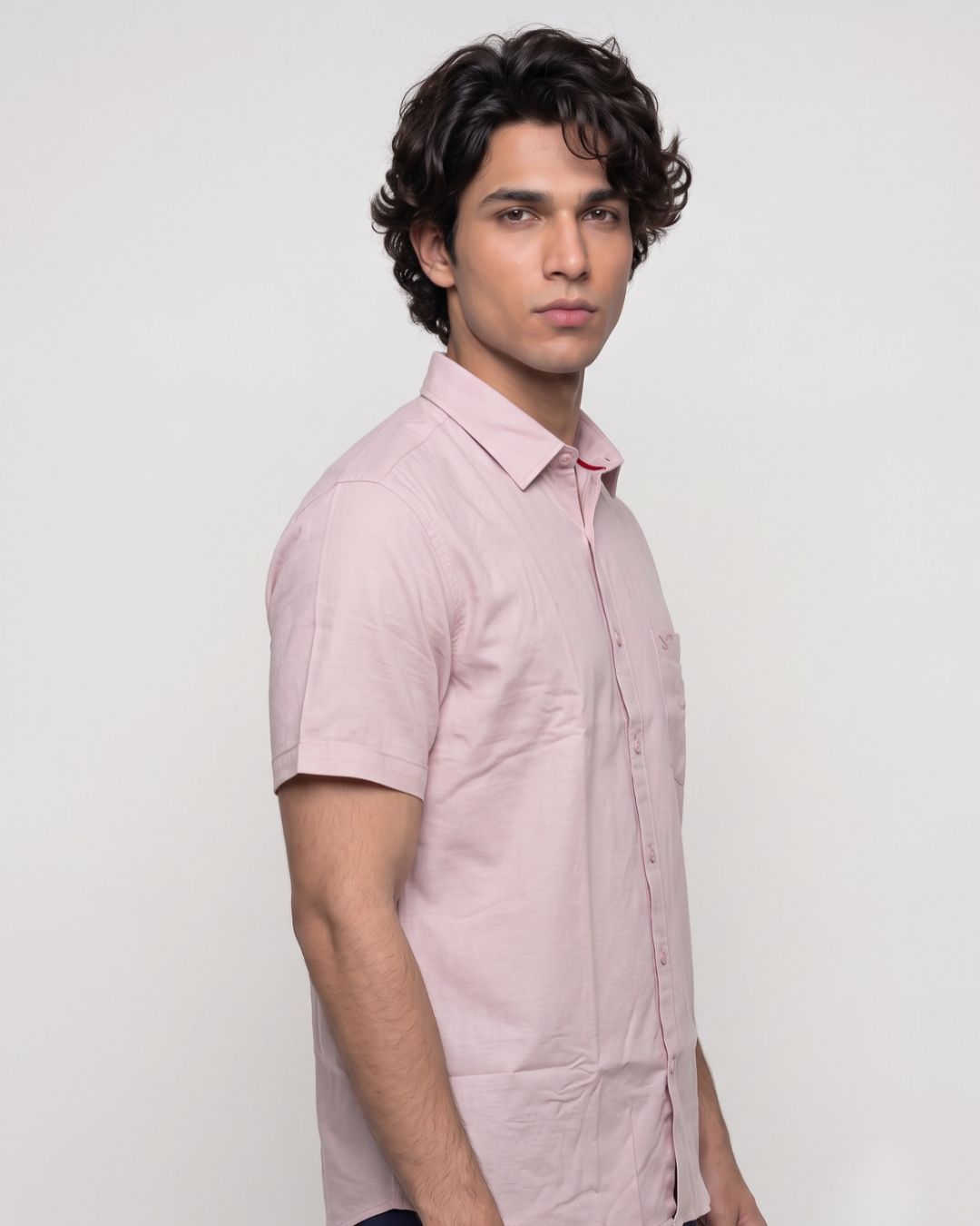 A man wearing a light pink short-sleeve button-up shirt, shown from a side profile against a plain light gray studio background.