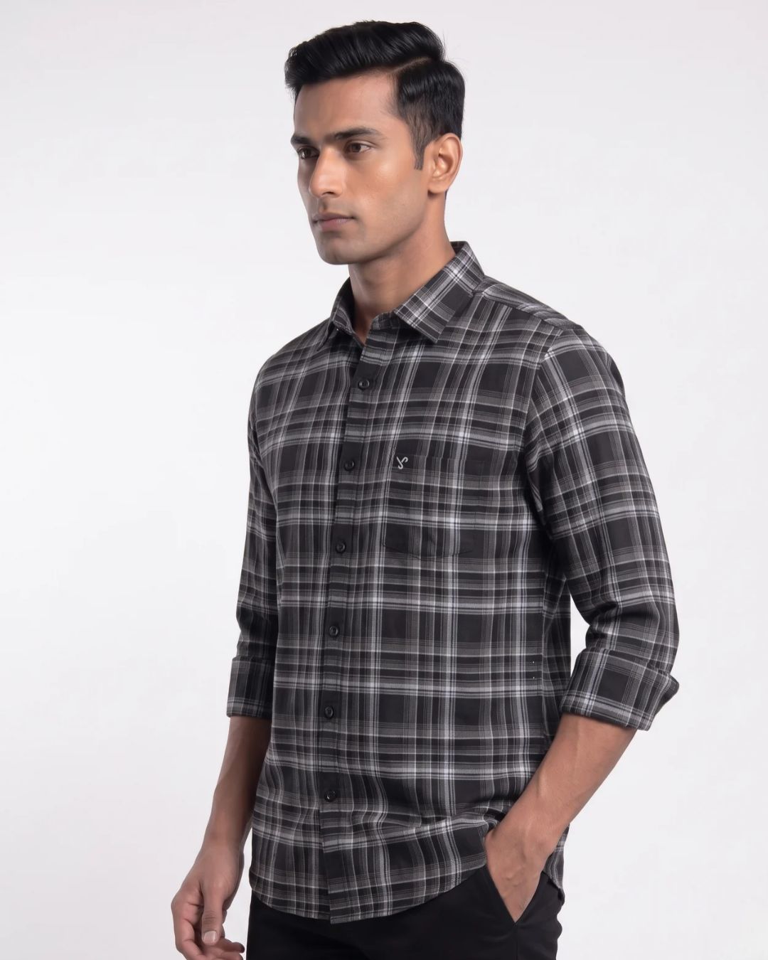A man wearing a black and gray plaid long-sleeve button-down shirt, shown from a side profile against a plain white studio background.