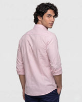 A man wearing a light pink long-sleeve linen shirt with rolled-up sleeves, shown from a three-quarters back view against a plain light gray background.