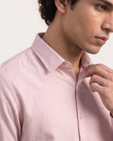 A close-up of a man wearing a light pink long-sleeve button-down dress shirt, adjusting the collar with one hand.