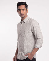 A man wearing a light beige long-sleeve button-down shirt with a small white floral pattern, posed against a plain white studio background.