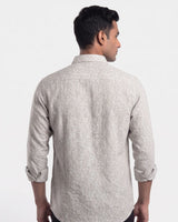 A man viewed from the back wearing a light beige long-sleeve shirt with a subtle white micro-pattern, set against a plain white studio background.