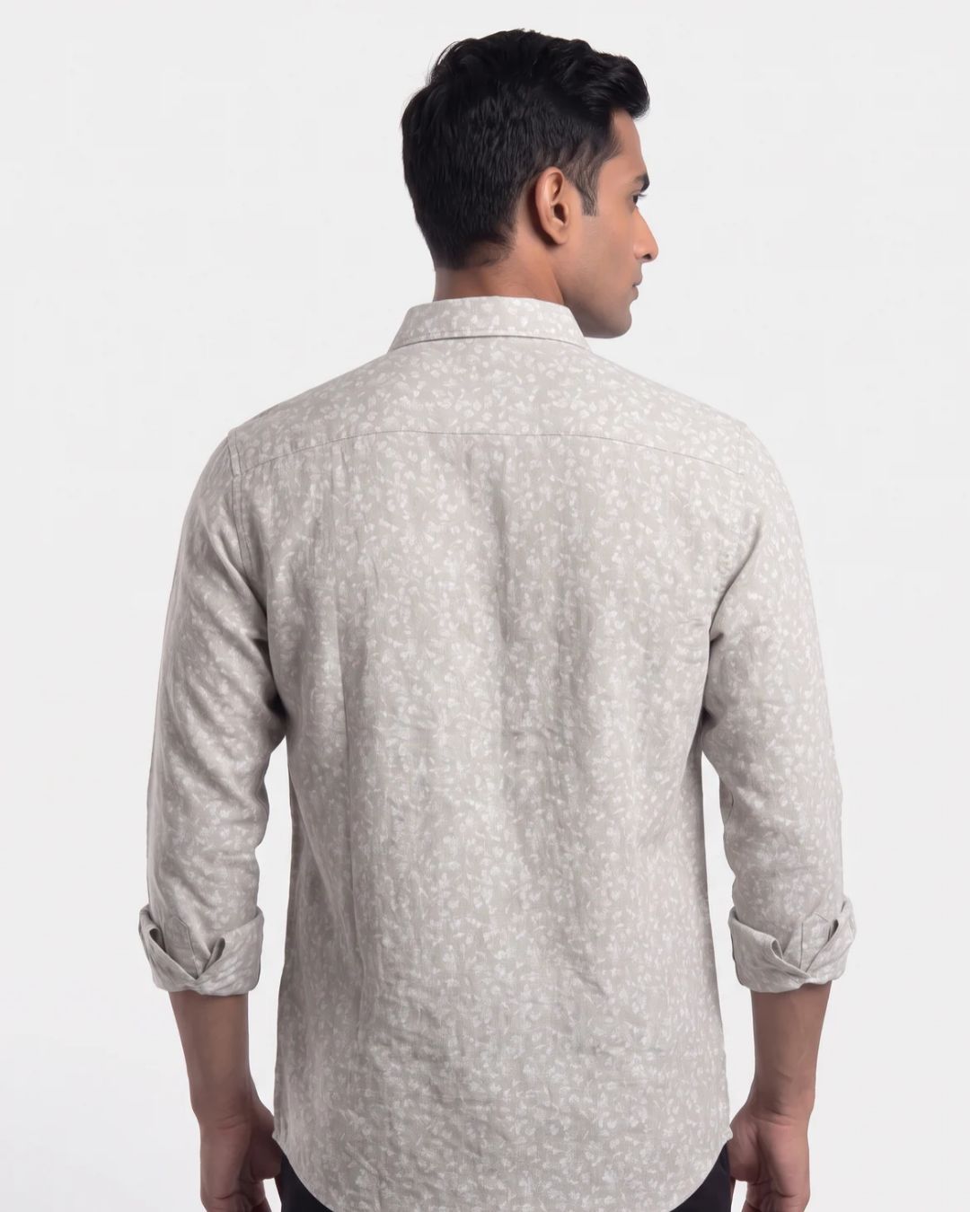 A man viewed from the back wearing a light beige long-sleeve shirt with a subtle white micro-pattern, set against a plain white studio background.