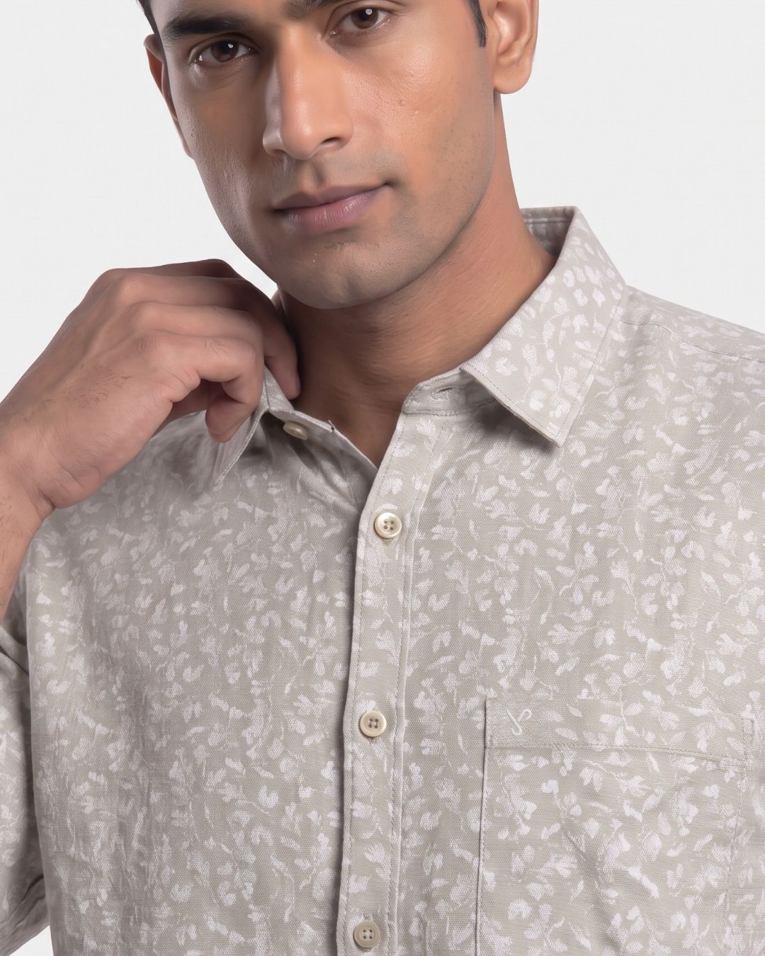 A close-up of a man wearing a light beige short-sleeve button-up shirt with a subtle white floral pattern, adjusting the collar.